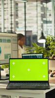 Vertical Green screen mockup laptop next to accountant inputting financial figures on PC after checking reports. Chroma key notebook next to businesswoman working in office, crosschecking data, camera B video