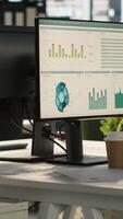 Vertical Modern office workspace desk with computer monitors displaying graphs, charts and data analytics, surrounded by plants and paperwork with city environment background, handheld camera shot video