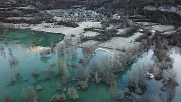 Aerial shot - Turquoise waters mirroring winter sunrise, frosted landscape surrounding Ibon de los Banos village, bare trees framing scenic mountain backdrop video