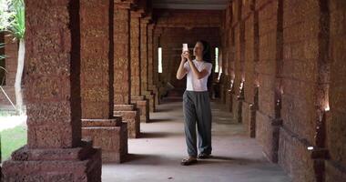 Handheld shot, Asian female tourist wearing wireless headphones listening to music while walking around the temple grounds. video