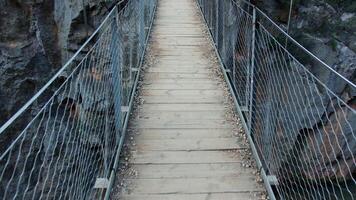Crossing wooden suspended bridge with metal netting, offering panoramic view of rocky gorge while experiencing adventurous hiking journey through breathtaking mountain landscape video