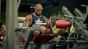 In modern gym environment bald athletic man beard focuses intently while performing leg exercises on does leg extensions. His dedication illustrates commitment fitness video