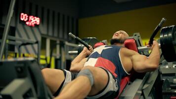 athletic bald man beard focuses intensely as he completes leg press exercises in gym during evening. Weights are positioned on machine as he pushes upward video