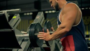 bald athletic man beard focuses on leg exercises using weights in well equipped gym. He hangs weights on leg press machine video