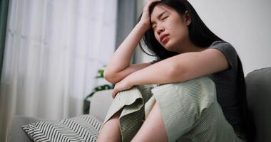 Handheld low angle view shot, Stressed Asian woman sits alone on a sofa, thinking aimlessly, feeling worried about something. Life problems video