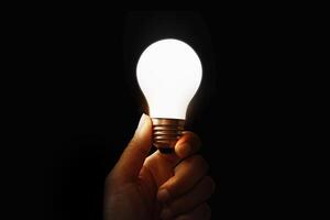 Hand holding illuminated light bulb, concept creativity on black background. photo