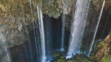 Powerful waterfall cascading over rocky cliff edge, plunging into turquoise water pool, surrounded by verdant moss and greenery in scenic turkish landscape video