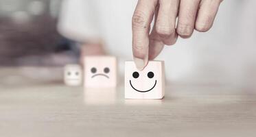 Customer services best excellent business rating experience. Satisfaction survey concept. Hand of a businessman chooses a smiley face on wood block cube photo