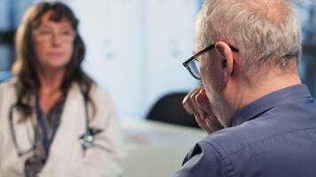 Old man in wheelchair coughing and dealing with a respiratory problem, flu symptoms at checkup with medical expert. Patient with disability suffering from asthma or throat infection. Camera B. video