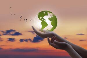 hands holding a green globe against a sunset sky photo