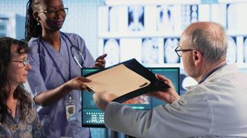 Oncology consultation takes place as a senior medic explains radiology scan, emphasizing preventive medicine and healthy lifestyle recommendations. Shares risk factors and causes. Camera B. video