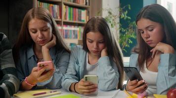 Boring addict four teens pupils classmates students using smartphones apps internet bored addiction online dependency overuse teenagers scrolling mobile phones social media in school library gen z video