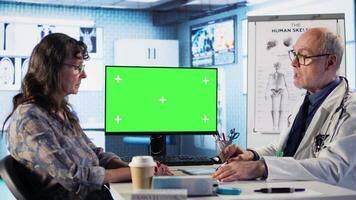 Experienced physician doing check up routine with patient next to chroma key screen, discussing about medicine and wellness. Old woman using health insurance for consultation with medic. Camera A. video