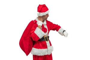Santa Claus checking the time on his wristwatch while holding a bag of gifts white background photo