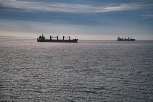 Two cargo ships glide across a calm sea under a clear sky. photo