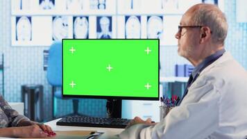 Experienced physician doing check up routine with patient next to chroma key screen, discussing about medicine and wellness. Old woman using health insurance for consultation with medic. Camera B. video