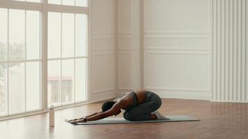 A woman performs a yoga stretch in an elegantly designed indoor space, focusing on her flexibility and mindfulness. The light-filled room encourages a calming atmosphere for her workout. video