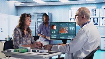 Physician highlights MRI scan advising on cancer treatment options and preventative health strategies for a geriatric patient. Medic and patient reviewing tumor growth, risk factors Camera A. video
