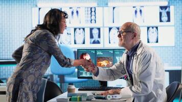 vecchio specialista incontro con un' donna paziente per discutere risultati nel un' mobiletto, utilizzando Avanzate diagnostico attrezzatura per interpretare X raggio scansioni e risultati, professionale assistenza sanitaria approccio. telecamera b. video