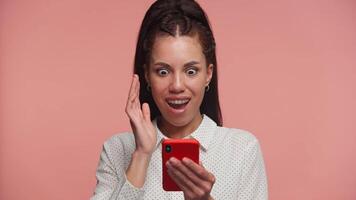 Surprised woman reacting to shocking phone notification on pink video