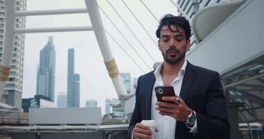 manager sta su strada con mobile Telefono e caffè. uomo è Tenere Telefono e digitando messaggi mentre assunzione rompere per Guarda in giro edifici. Telefono è non rilasciato a partire dal mani di attributo uomo d'affari. video