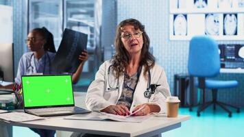 Experienced physician doing checkup routine with patient next to chroma key screen, discussing about medicine and wellness. Man using health insurance for consultation with medic. Camera B. video