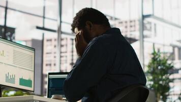 Worker feeling painful headache while working, suffering burnout while rushing to finish tasks before deadline. African american man in office having migraine after working overtime, camera A video