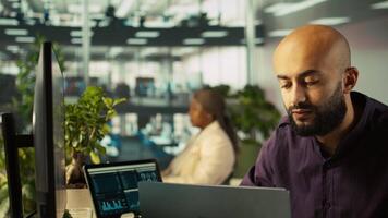 Smiling employee in warm office working on company project, multitasking. Cheerful freelancer answering emails, typing on keyboard, working in modern workplace, camera B close up video