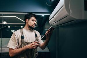 Technician performs maintenance on air conditioning unit while checking data on tablet photo