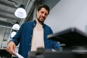 Man using a printer in a modern office space during working hours with bright overhead lighting photo