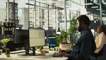 Employee reviewing financial charts at desk in modern office, analyzing business performance metrics. Professional at work looking over data trends and strategic insights, camera B video