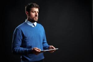 Man in blue sweater using tablet in a studio setting with a dark background during a casual indoor moment photo