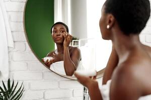 Skincare routine of a woman applying cream in a modern bathroom mirror during the evening hours photo