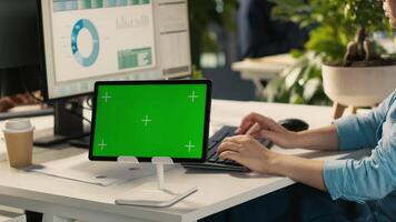 Close up of employee sitting at office desk, using green screen tablet to solve tasks during job shift. Office clerk doing email communication in workplace using chroma key device, camera A video