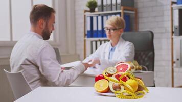 A healthcare professional discusses dietary recommendations with a man patient in a well-lit clinic. Fresh fruits are visible on the table, highlighting the focus on healthy eating and nutrition. video