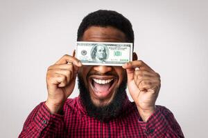 Easy Money. Happy Black Man Holding One Hundred Dollar Banknote In Front Of Face Posing On White Studio Background. Wealth And Income, Financial Success, Cash Greediness Concept photo