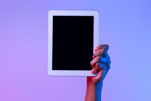 Male African American Hand Holding Digital Tablet With Black Blank Screen, Demonstrating Free Copy Space For Your App Design Or Advertisement Over Purple Studio Background In Neon Lighting, Mockup photo