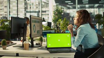 Green screen laptop on office desk next to employee editing documents on computer. Mockup notebook next to worker analyzing data charts, interpreting statistical information, camera B video