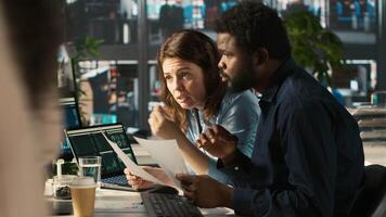 Manager at office desk next to accountant checking financial figures on documents, doing reports. Team leader and man working together crosschecking data on paperwork files, camera A video