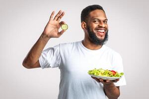 Joyful Black Man Holding Vegetable Salad Gesturing Okay Choosing Healthy Food Standing Over White Studio Background, Smiling To Camera. Slimming Nutrition And Male Weight Loss photo