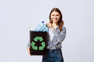 Positive Millennial Woman Holding Black Container With Empty Plastic Bottles For Recycling, Young Eco-Activist Lady Standing Over Light Studio Background, Smiling At Camera, Copy Space photo