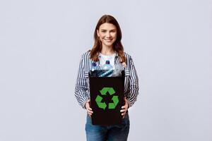 Beautiful Young Lady Carrying Container With Empty Plastic Bottles Ready For Recycling, Millennial Nature-Lover Woman Enjoying Zero-Waste Living, Standing On Light Studio Background, Copy Space photo
