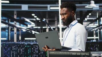 Data center system administrator analyzing infrastructure issues using node tree tools. Man in server hub using AI visualization insights on laptop to optimize system health, camera B video