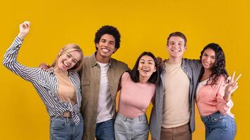 Friendship of international students and differ race pupils. Happy teens different people hugging, gesturing and expressing emotion of joy, isolated on orange background, studio shot, empty space photo