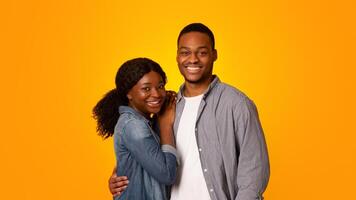 Portrait of cheerful young black couple embracing each other while posing over yellow background in studio, millennial african american man and woman hugging and smiling at camera, copy space photo