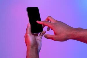Male Hands Using Smartphone With Black Screen In Neon Light Over Purple Background, Unrecognizable African American Man Touching Phone Screen, Browsing New App Or Scrolling Website, Mockup Image photo