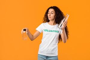 No More Plastic. Volunteer Lady Choosing Glass Bottle Instead Of Plastic Standing On Yellow Background. Ecology And Environment, Conscious Consumption Concept. Studio Shot photo