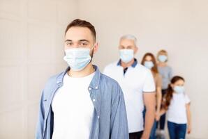Young guy in medical mask standing in line for coronavirus immunization at health centre, empty space. Antiviral vaccination and protection from infectious disease concept photo