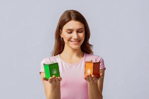 A woman displays two colorful recycling bins, smiling while encouraging eco-friendly practices. Her casual clothing and the neutral background set a positive tone for sustainability awareness. photo