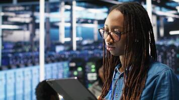 Vertical Portrait of smiling server room engineer using device to interpret data analytics graphs. Happy data center worker using artificial intelligence tool showing system metrics, camera B video